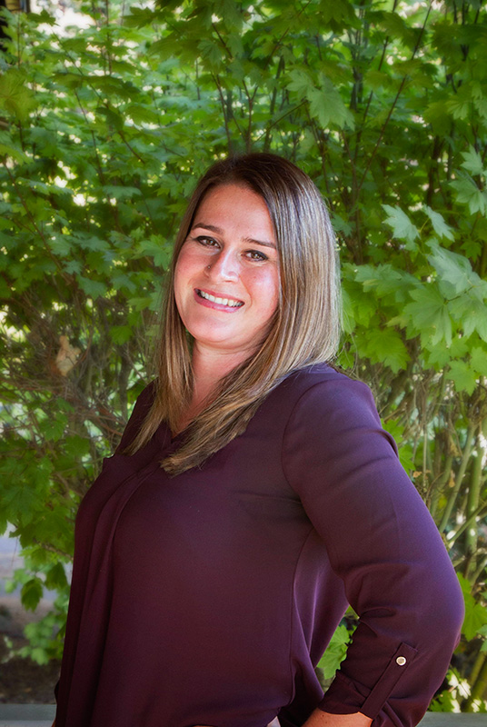 dr-kristin-costanzo-headshot Professional headshot of a chiropractor at Fox and Fern Chiropractic in Bemidji, MN, smiling in front of a natural green foliage background.
