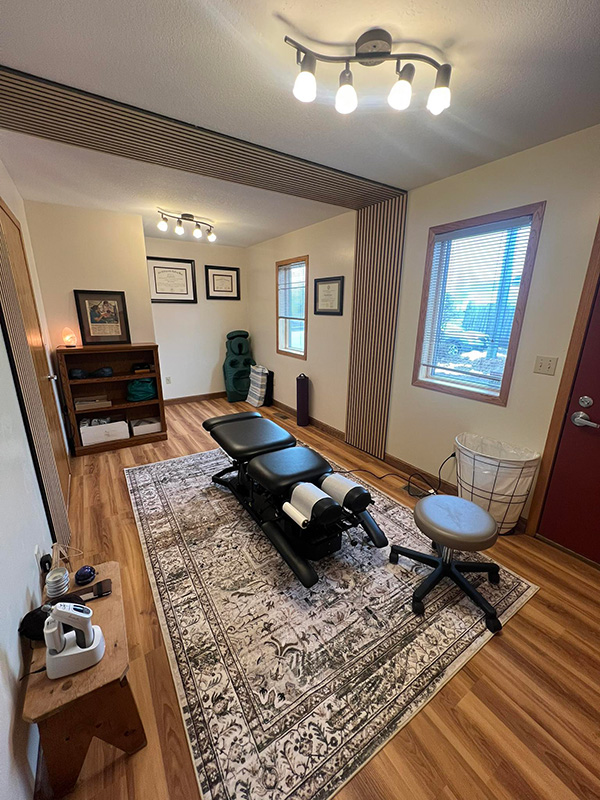 fox-and-fern-chiropractic-treatment-room The welcoming treatment room interior at Fox and Fern Chiropractic in Bemidji, MN, featuring a professional black chiropractic adjustment table, warm lighting, and a patterned area rug.