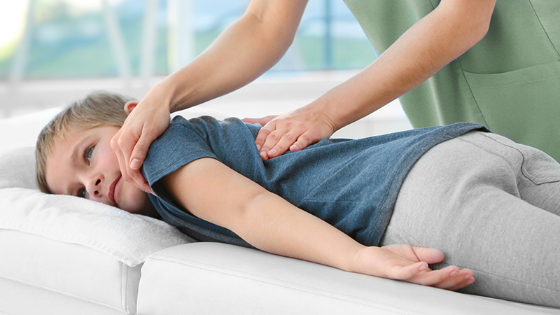 pediatric-chiropractic-adjustment A young boy lying on his side receiving a gentle pediatric chiropractic adjustment on his spine at Fox and Fern Chiropractic in Bemidji, MN.